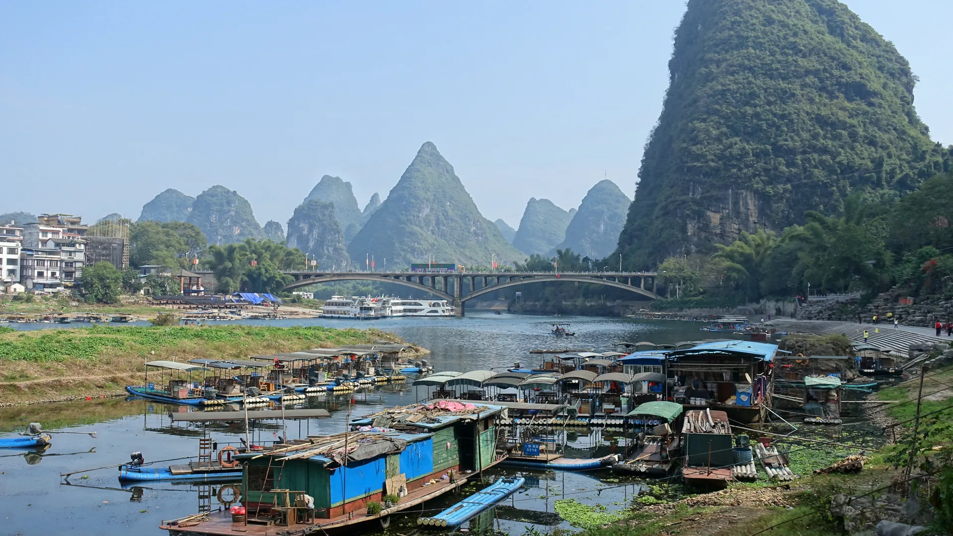 The Li River bend at Yangshuo with jagged karst peaks rising behind the bridge and moored river boats along the bank